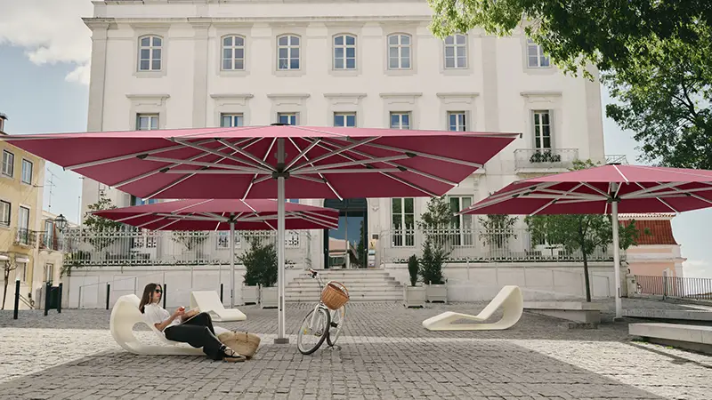 Grosse Sonnenschirme auf gepflastertem Platz vor Gebäude – Beschattung für öffentliche Bereiche